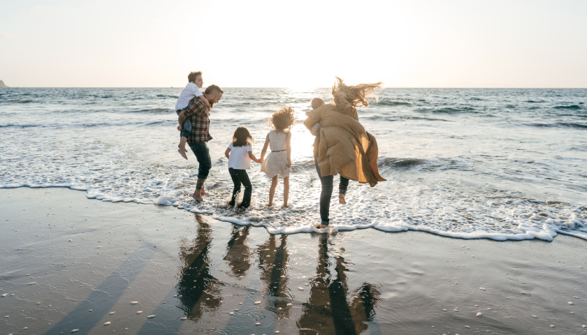 Family on sandy beach running into ocean.